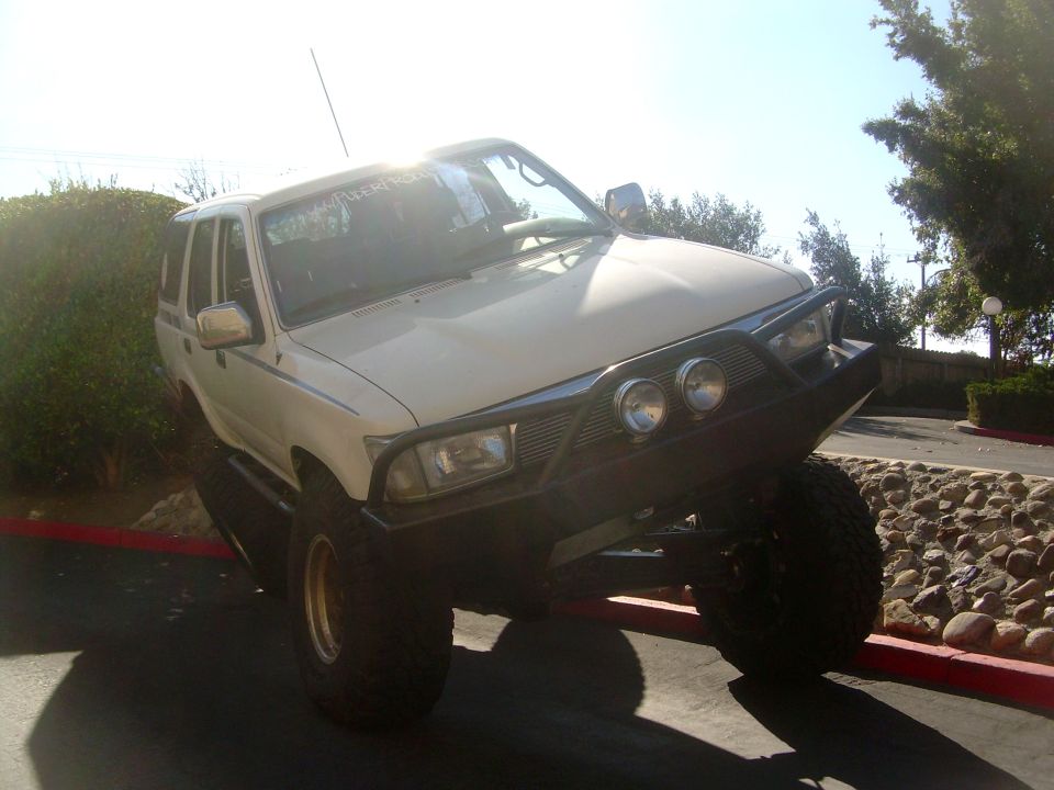 White 1993 Toyota 4Runner with aftermarket bumper and large tires, parked on an incline
