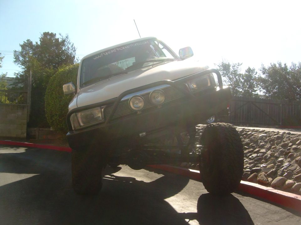 White lifted SUV flexing front tire up on a curb, low-angle backlit front view