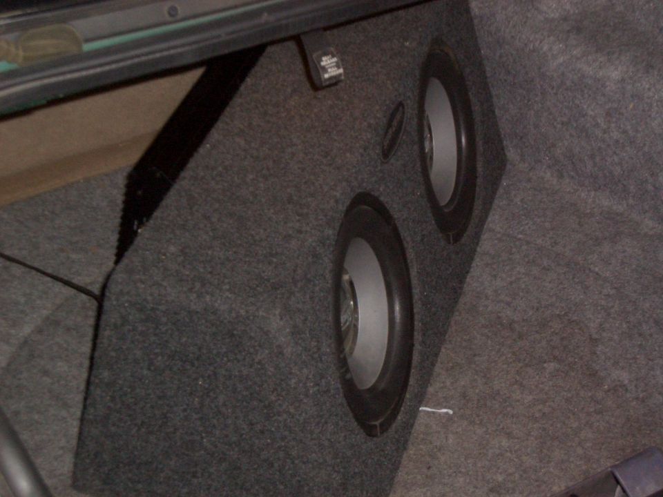 Two subwoofers in a custom carpeted enclosure inside a cargo area
