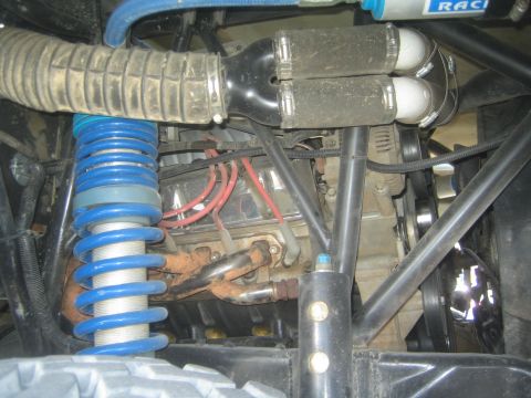 1990 Ford Bronco - Engine-bay detail of an off-road truck showing a blue coil spring, exhaust header, red wiring and tubular chassis framing.
