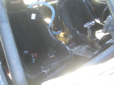 1990 Ford Bronco - Interior of an off-road race truck with black MasterCraft bucket seats, harnesses, a center shifter and steering wheel inside a roll cage.