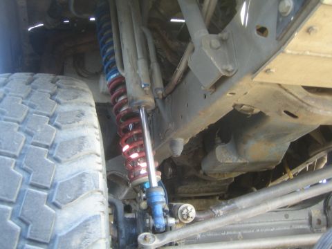 1990 Ford Bronco - Suspension detail of an off-road truck with a blue-and-red coilover shock, frame rails and a large tire at the wheel.