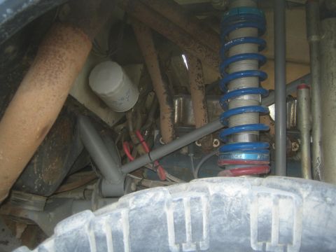 1990 Ford Bronco - Close-up of a blue coilover spring and weathered tubular chassis components mounted above a dusty mud-terrain tire.