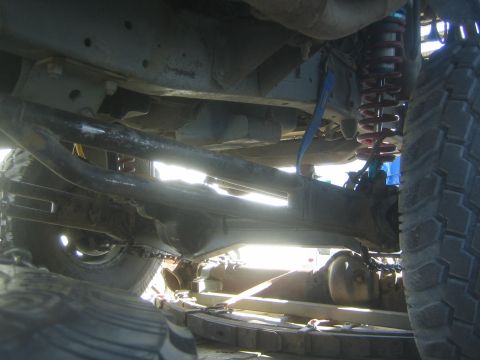 1990 Ford Bronco - Strongly backlit undercarriage of an off-road truck showing the axle, a red coil shock and tie-down chains on a trailer deck.