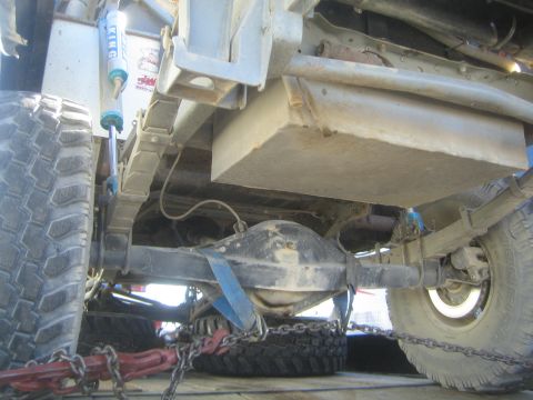 1990 Ford Bronco - Undercarriage view showing a skid-mounted fuel tank, leaf springs, a blue shock and rear axle beneath an off-road truck.