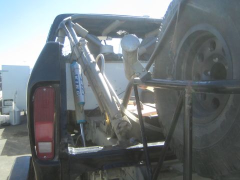 1990 Ford Bronco - Rear view into the bed of an off-road truck showing the tubular cage, blue bypass shocks and a mounted spare wheel.