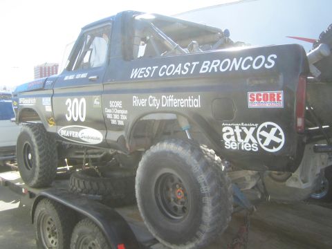 1990 Ford Bronco - black classic Ford Bronco race truck #300 lettered West Coast Broncos and River City Differential, parked on a flatbed trailer.