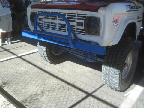1990 Ford Bronco - Side-front view of a white-and-red early Ford Bronco off-road racer with a blue Class3Racing.com tube bumper and BFGoodrich tires.