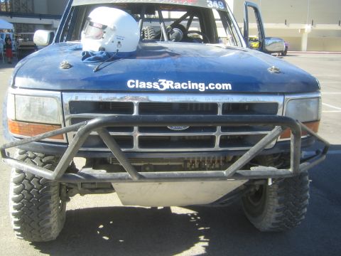 1990 Ford Bronco - Front view of a blue Ford off-road racer #349 with a helmet on the hood, Class3Racing.com lettering, tube bumper and skid plate.