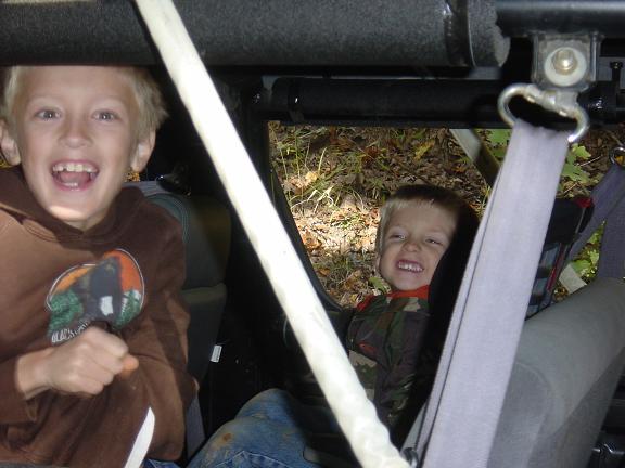 Two smiling boys in a vehicle interior, one in a brown hoodie, the other in camouflage