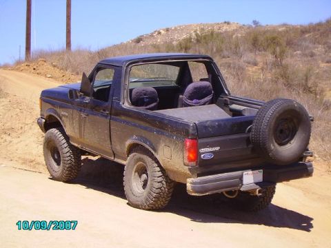 1990 Ford Bronco - This black 1990 Ford Bronco is equipped with off-road tires and a spare tire mounted on the rear, seen on a dirt road.