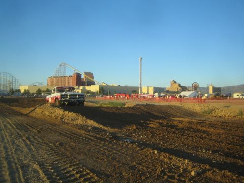 1990 Ford Bronco - black-and-white pickup truck rests on a dirt track berm at golden hour, with an amusement park skyline across the course.