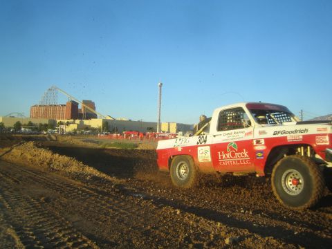 1990 Ford Bronco - red-and-white off-road race truck lettered HotCreek Capital and number 304 kicks up dirt through a corner on a short-course track.