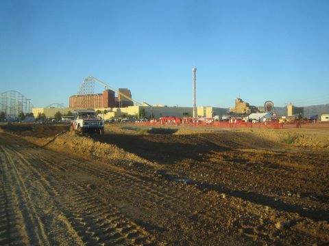 1990 Ford Bronco - off-road truck rests on a dirt track berm at golden hour, with a roller coaster and amusement park buildings across the course.