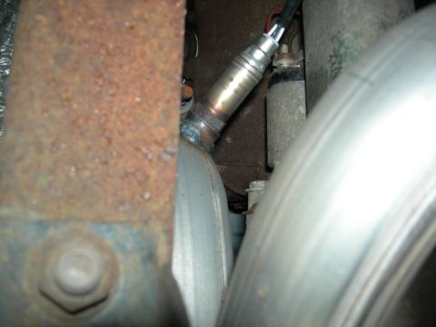 1996 Ford Bronco - Close-up view of an oxygen sensor installed in an exhaust system, showing rusty metal components and shiny pipes.