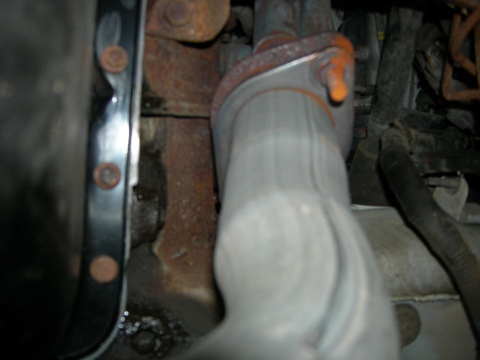 close-up of exhaust pipe connection to engine block with rusty metal parts and wiring