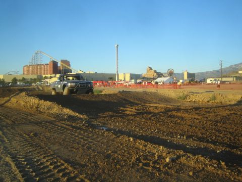 1990 Ford Bronco - off-road truck navigates a churned dirt berm with a casino, roller coaster and Ferris wheel skyline behind orange course fencing.