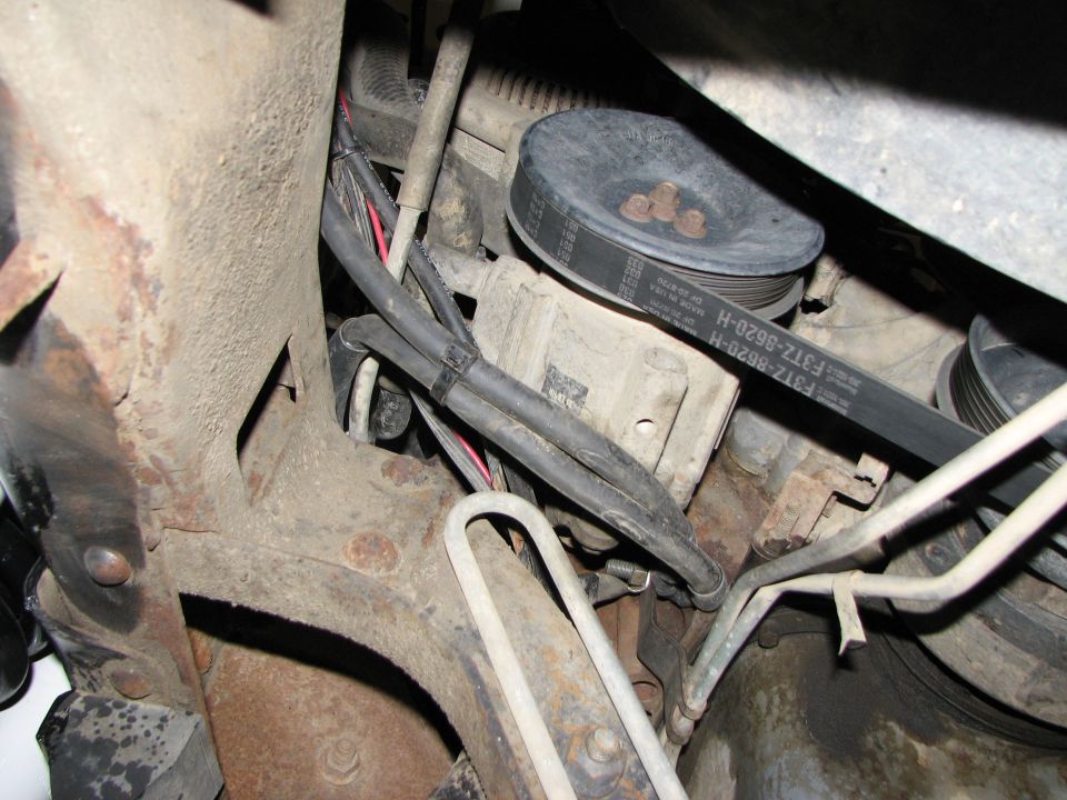 Engine bay close-up of serpentine belt marked F31Z-8620-H around pulleys with hoses and rusty frame parts