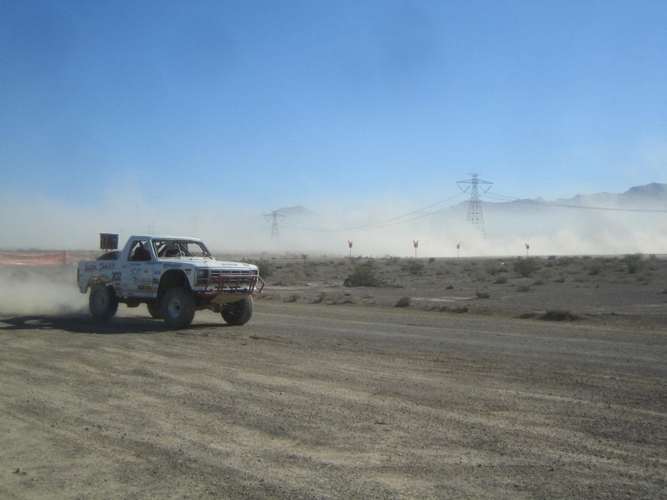 White race truck launching off a rise on a desert dirt course
