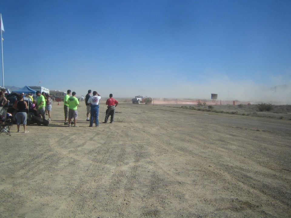 Spectators watching a distant race truck raise dust on a desert course