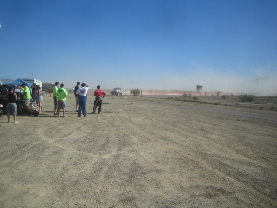 Spectators at a desert race course with a truck and dust in the distance