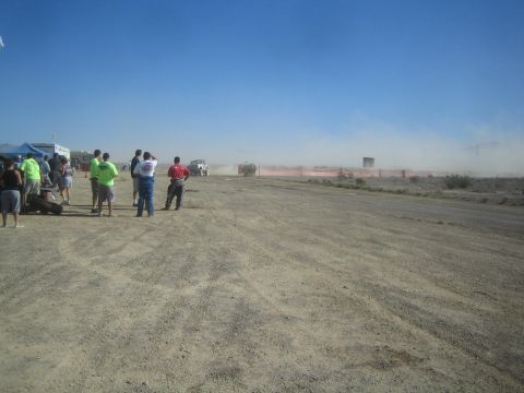 1990 Ford Bronco - crowd of onlookers watches a race truck throw up dust along a red-bordered desert dirt course.