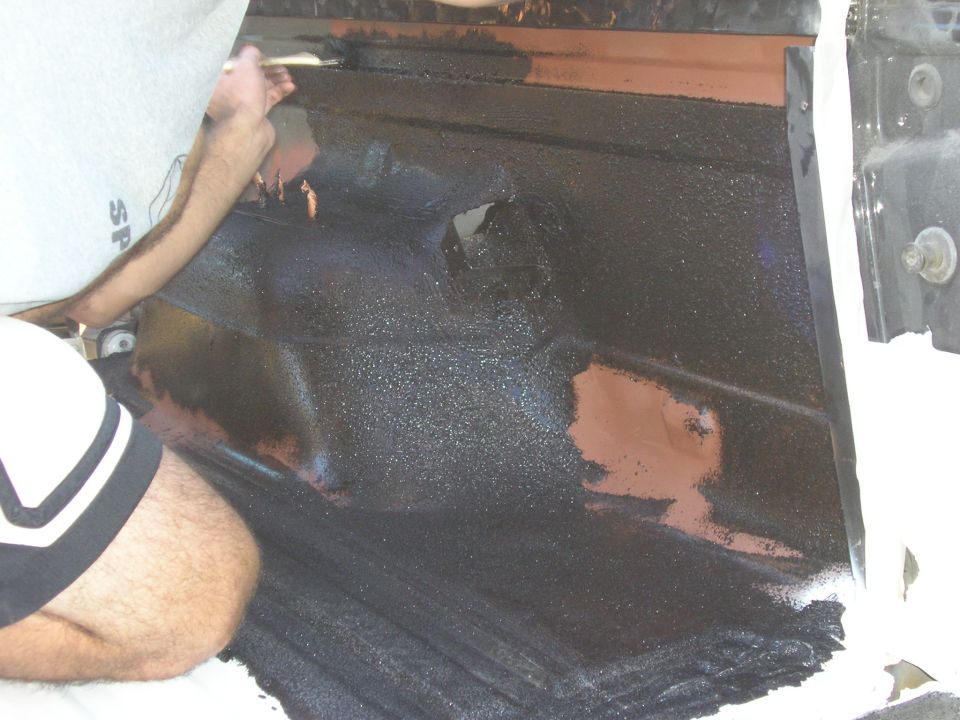 Person brushing black bedliner coating onto a stripped truck cab floor pan