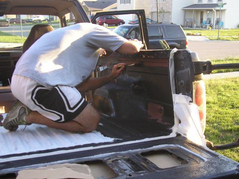 1996 Ford Bronco - Man applies a protective coating to the interior of a truck bed, with other vehicles visible in the background.