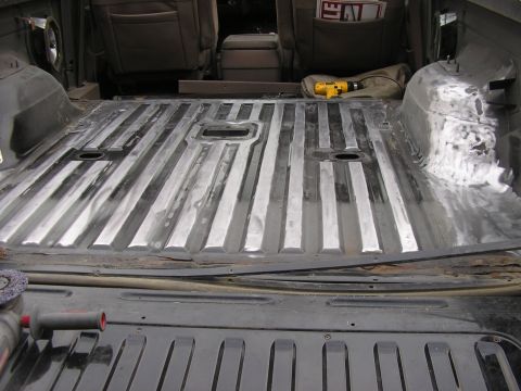 1996 Ford Bronco - Looking forward into a stripped SUV cargo area with the rear carpet pulled out, exposing the ribbed bare metal floor sanded down to shiny s…