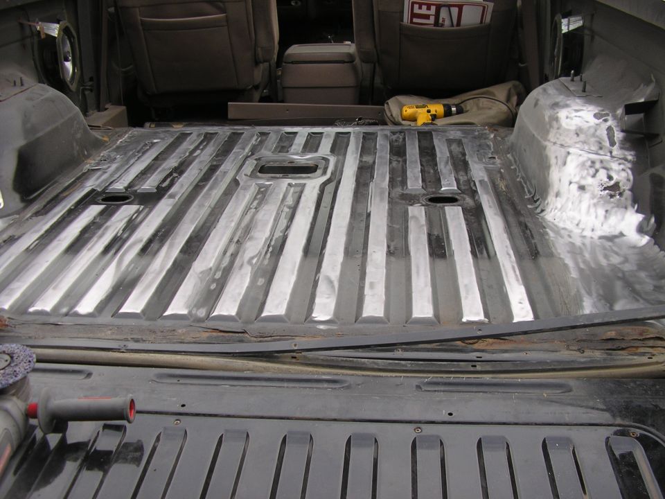 Stripped SUV cargo floor sanded to bare ribbed metal with drill and grinder