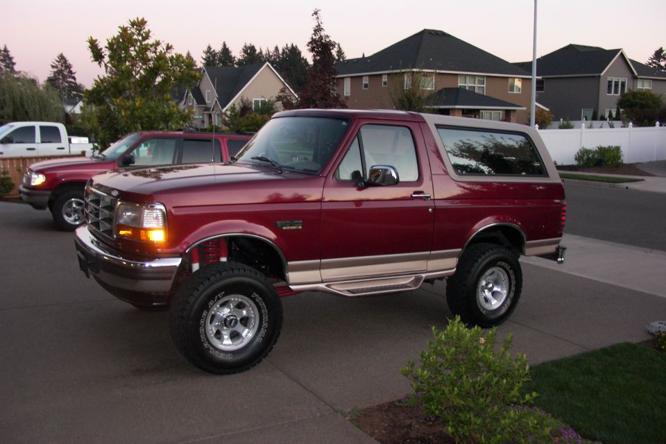 Maroon 1996 Ford Bronco with tan top, lifted suspension, and chrome wheels parked on driveway