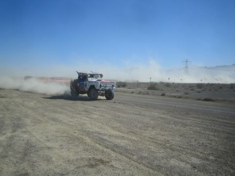 1990 Ford Bronco - white off-road race truck with a short open body races across a desert dirt course, trailing a long dust cloud.