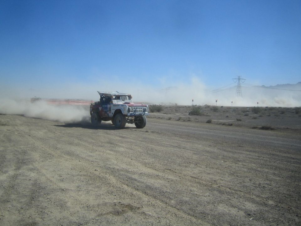 White early-Bronco-style race truck trailing dust in the desert