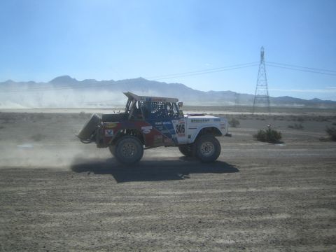 1990 Ford Bronco - white and red Bronco-style off-road race truck numbered 305 catches air on a desert dirt course near power lines.