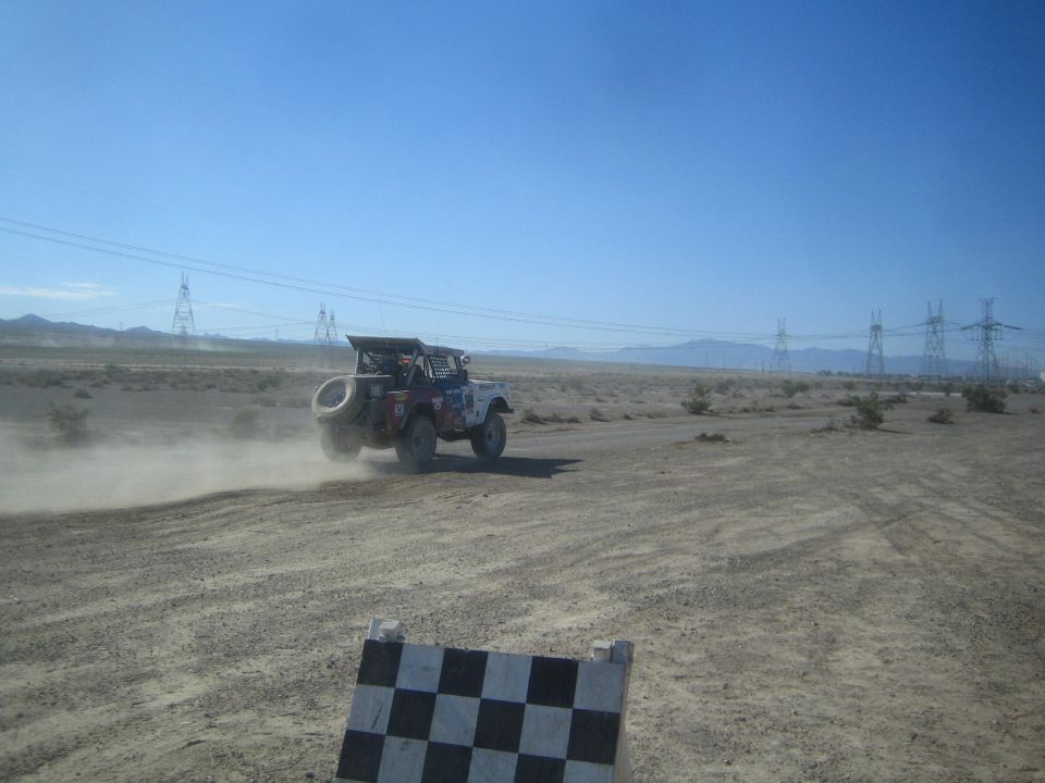 Race truck with spare tire on a desert track behind a checkered marker