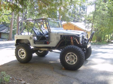 1986 Ford Bronco - This modified off-road vehicle is seen from a three-quarter front angle, with a roll cage and oversized tires.