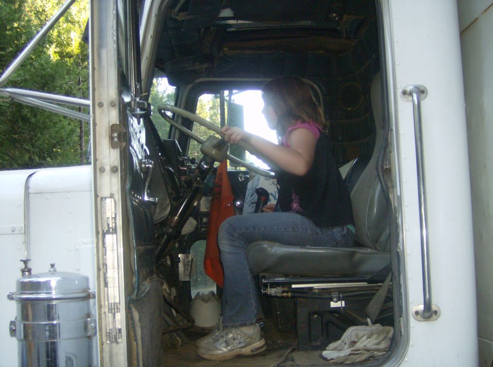 Girl sits in driver's seat of a large truck, holding the steering wheel