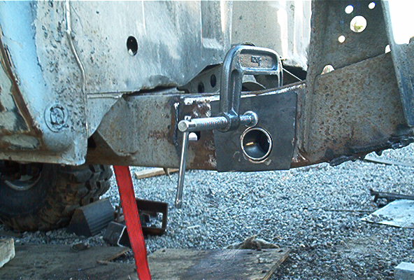 Rusty vehicle frame section with a C-clamp attached to a metal plate