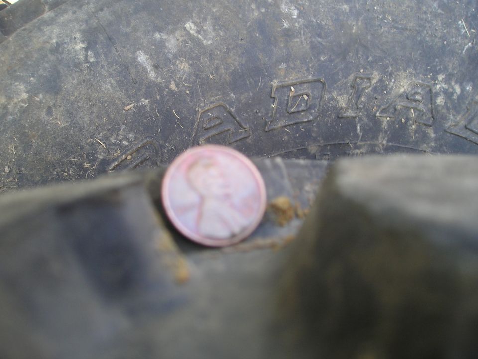 Close-up of a tire tread with a penny for scale, showing embossed lettering