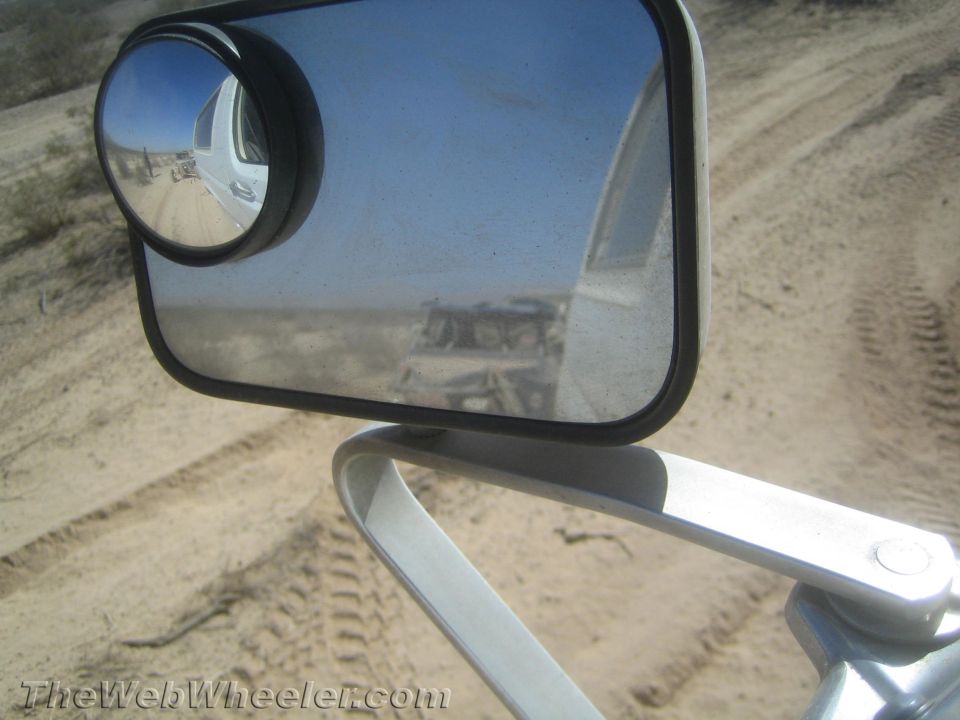 Side mirror reflecting a desert trail behind an off-road vehicle
