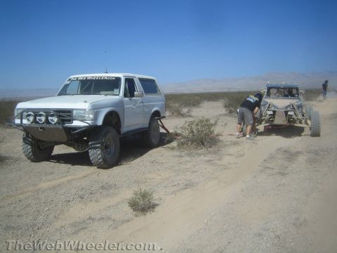 1990 Ford Bronco - White full-size Ford Bronco is hooked to recover a tube-chassis off-road buggy as a person works between them in open desert.