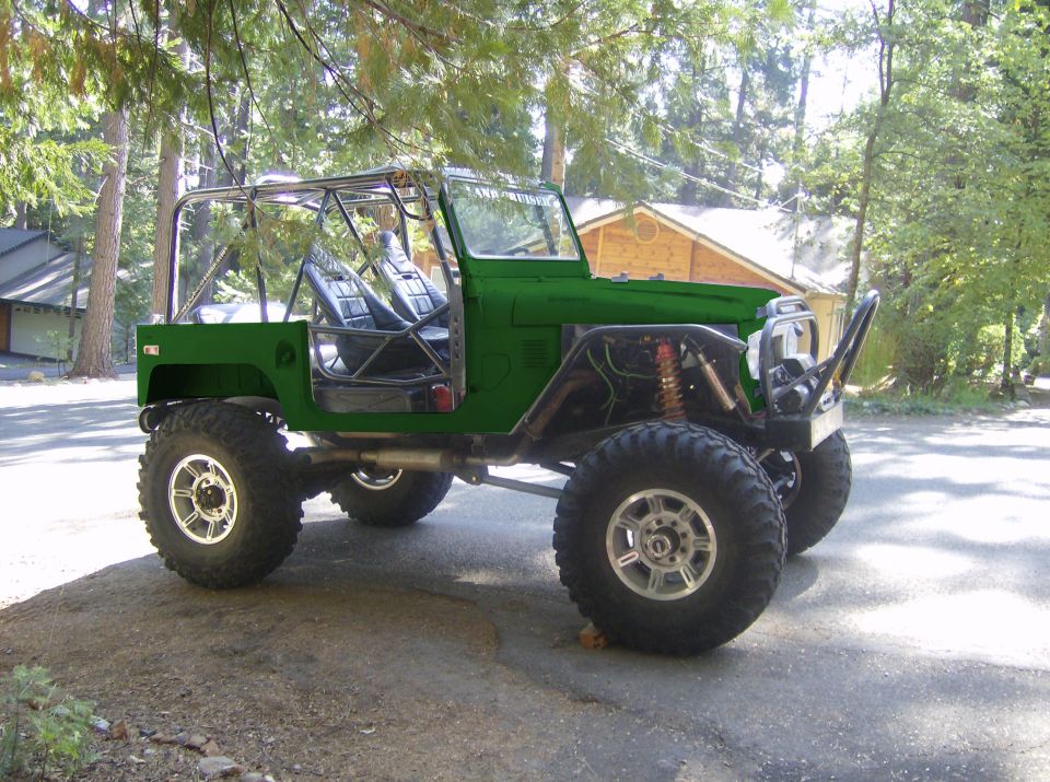 Green off-road vehicle with roll cage and large tires parked on asphalt