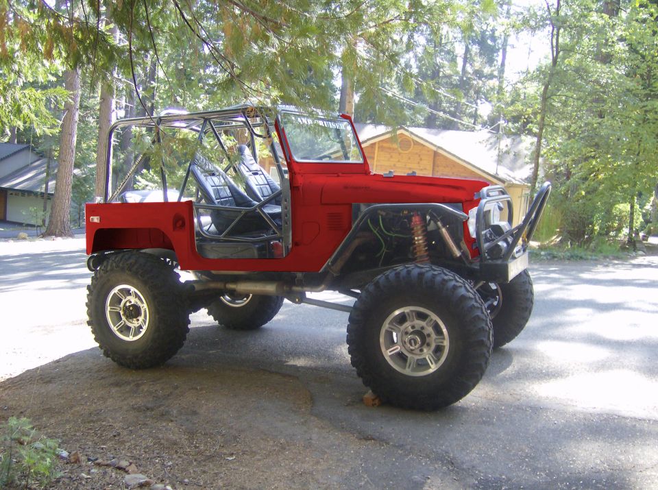 Red off-road vehicle with large tires, exposed engine components, and a roll cage. It has aftermarket bumpers and seats