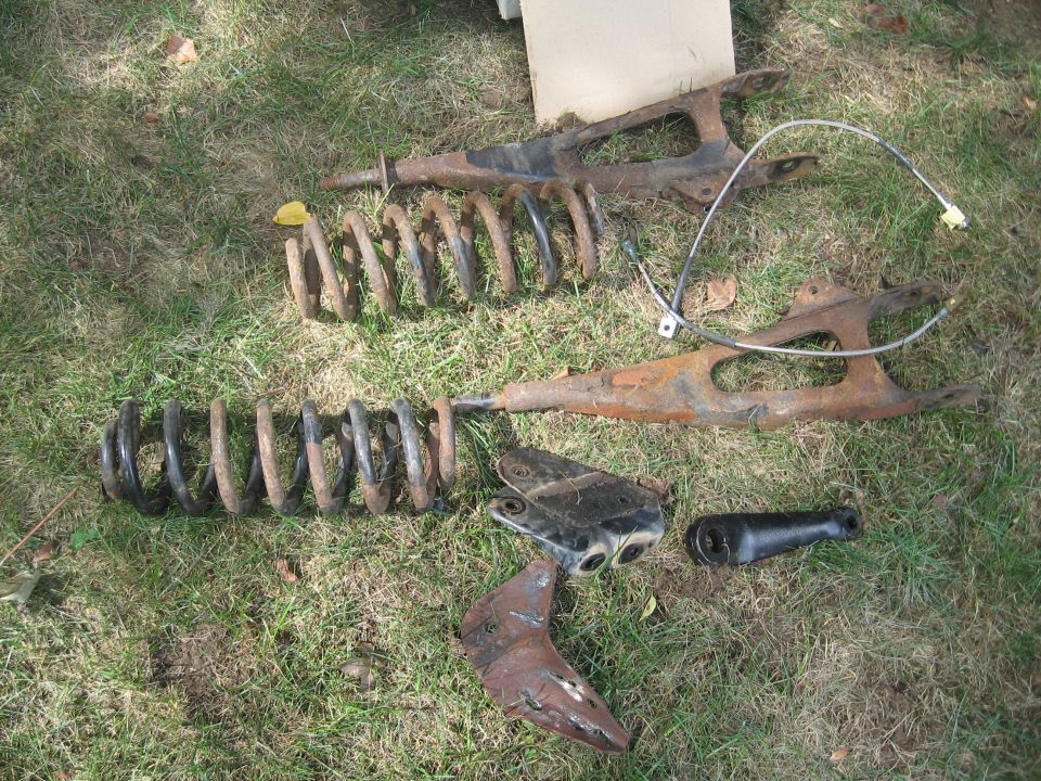 Rusty front suspension parts, including control arms and coil springs, laid out on grass