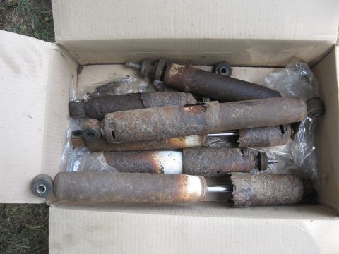 1996 Ford Bronco - A collection of heavily corroded shock absorbers are piled inside a cardboard box.