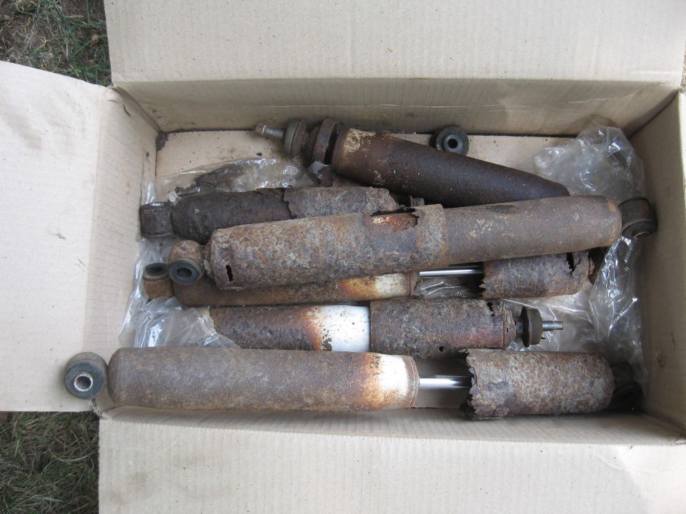 Cardboard box full of rusty used shock absorbers with exposed chrome shafts