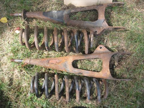 1996 Ford Bronco - Two rusty front suspension control arms with coil springs, likely for an older truck or SUV.