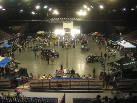 1990 Ford Bronco - Overhead view of an indoor arena floor packed with off-road vehicles, vendor booths and crowds at a motorsports event.