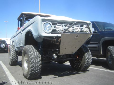 1990 Ford Bronco - Front three-quarter view of a white early Ford Bronco off-road rig with Hella lights and tube bumper parked in a lot.