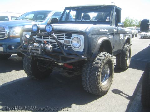 1990 Ford Bronco - Blue early Ford Bronco off-road rig with front winch, round driving lights and oversized tires parked in a paved lot.